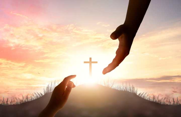 silhouette of two hands reaching toward each other with a cross in the background, symbolizing divine connection and the image of God.